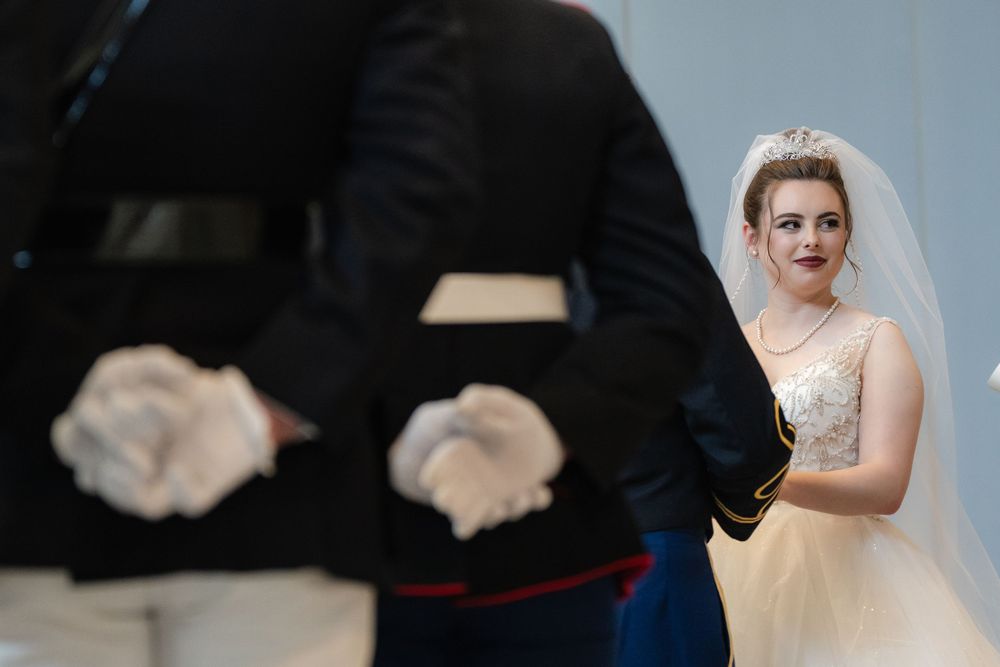 A bride in a vintage-style lace dress poses next to a person in a dark military uniform during an elegant wedding ceremony.