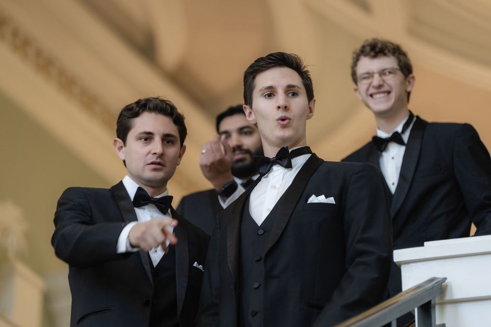 A group of men in formal black tuxedos and bow ties stand together at an elegant event.