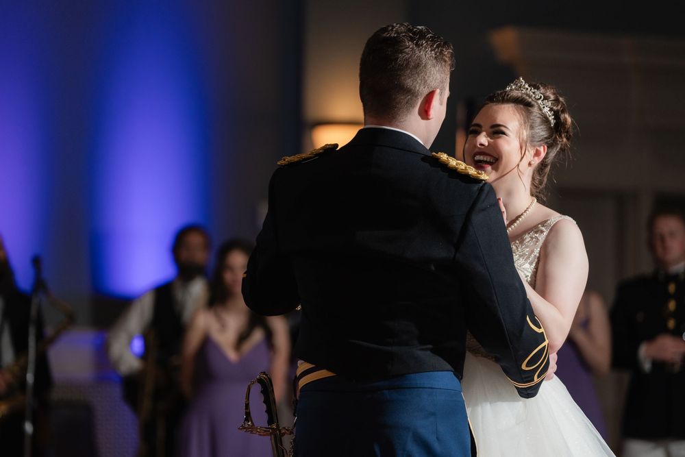 A romantic first dance at a wedding reception with blue uplighting in the background and guests watching.