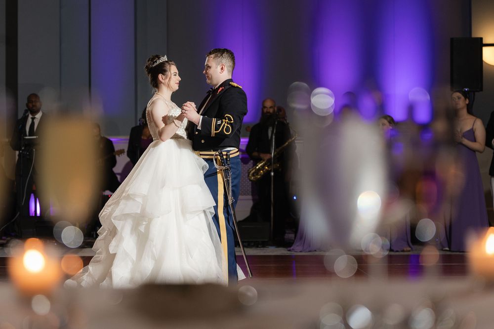 A couple shares their first dance at their wedding reception with purple lighting and candlelit ambiance.