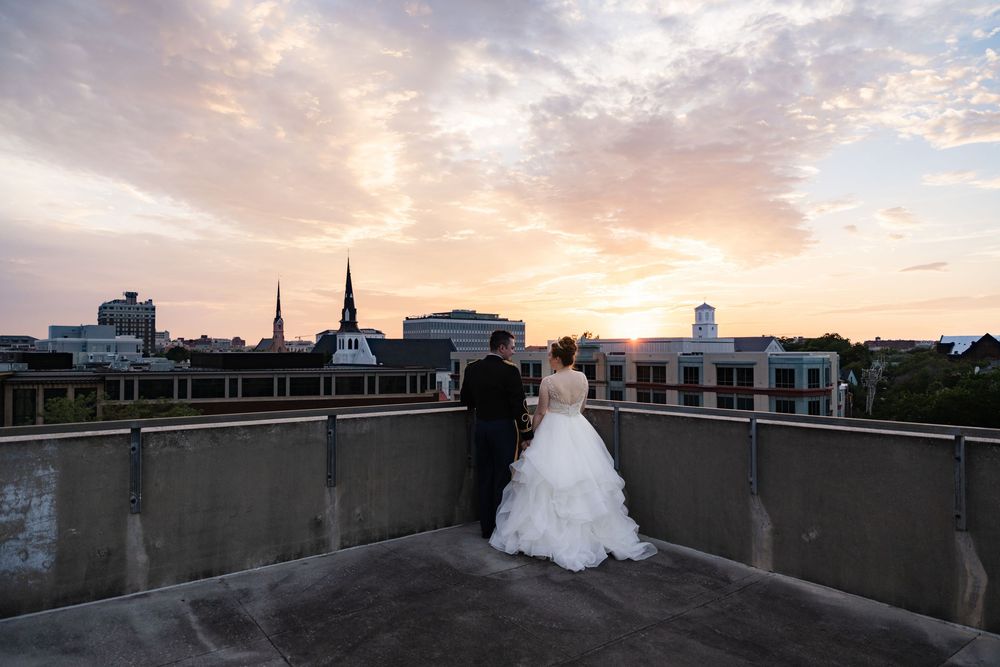 A couple stands on a rooftop overlooking Charleston, SC silhouetted against a dramatic sunset sky.