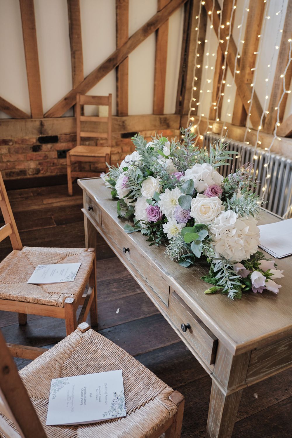 Beautiful wedding floral arrangement with white hydrangeas and greenery on rustic wooden table with wooden chairs nearby.