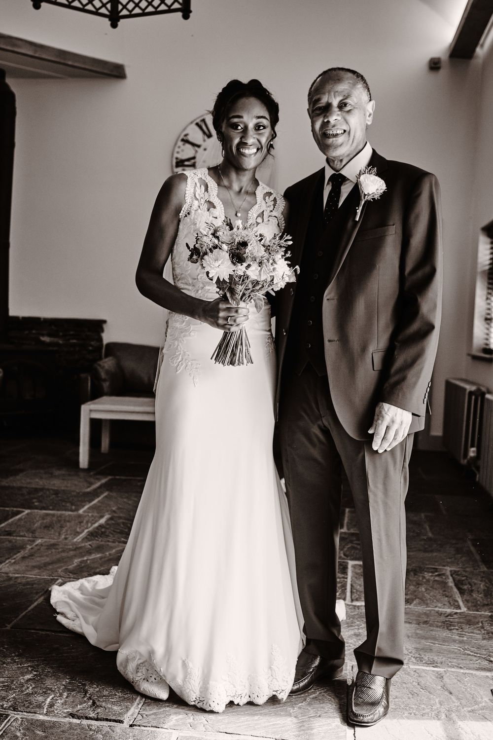 A black and white wedding photo showing a smiling bride in a white dress with a bouquet next to a person in a dark suit.