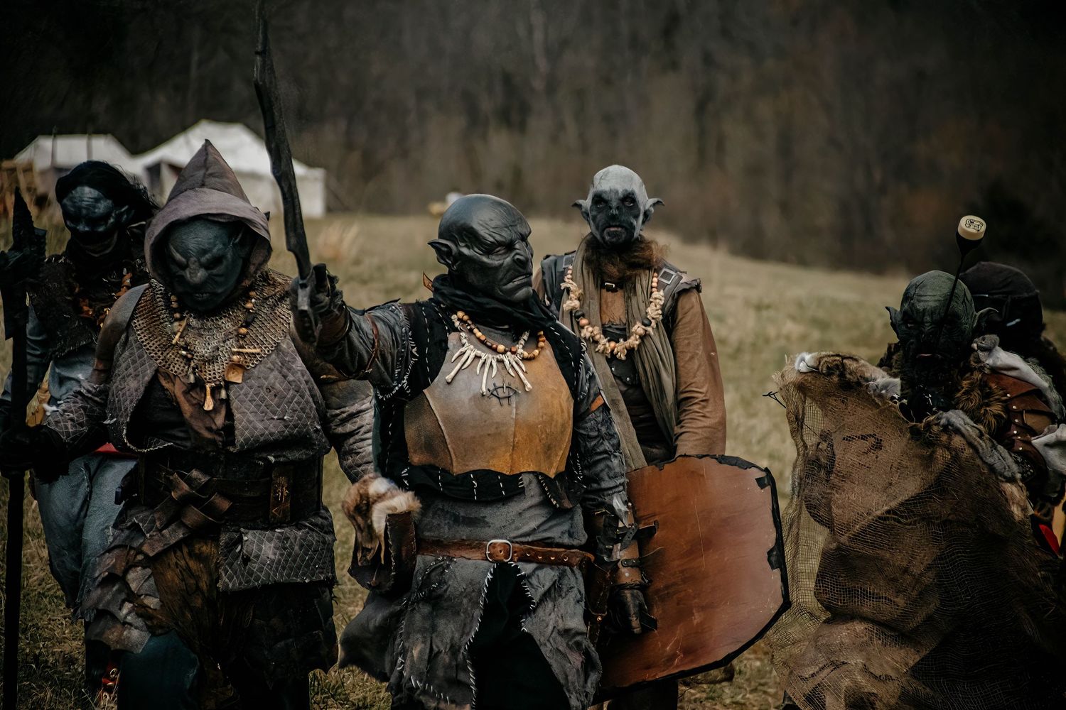 Post-apocalyptic cosplayers in orc masks and tattered armor gather in a wasteland-inspired outdoor setting.