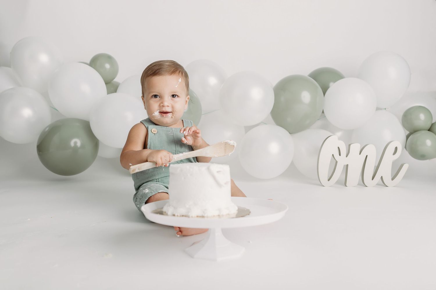 A baby in a pink tulle dress celebrates their first birthday with balloon decorations in soft pink, white and rose gold.