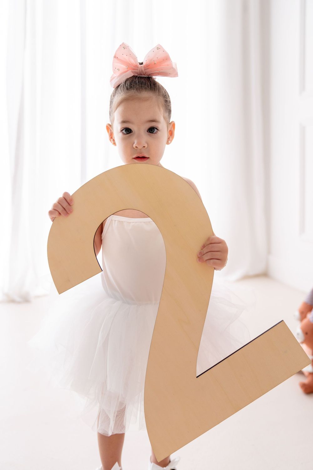 Small dancer in white tutu and pink hair bow holds large number 2 cutout.