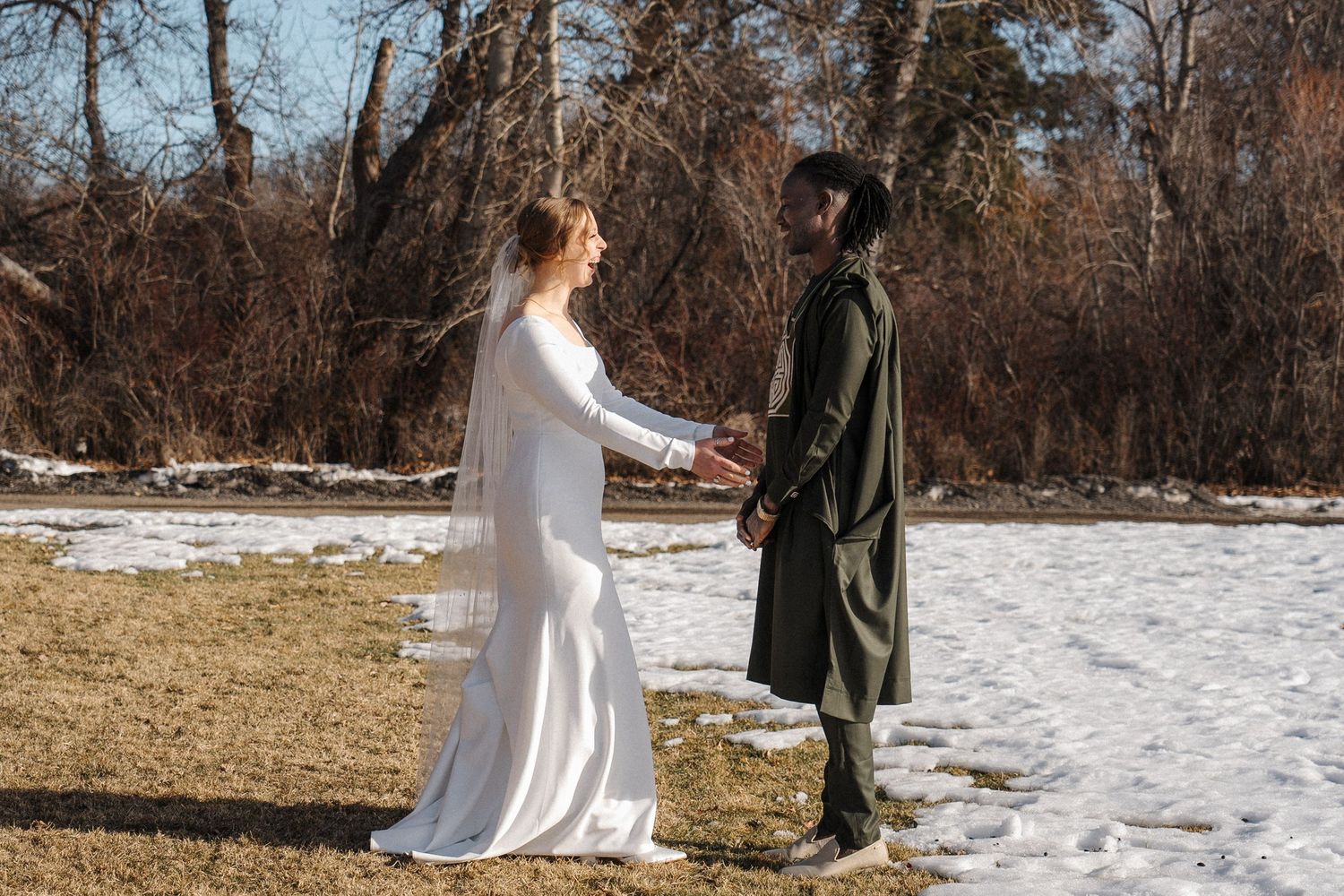 Winter wedding scene with two people standing in contrast between snowy ground and brown grass in a rustic outdoor setting.