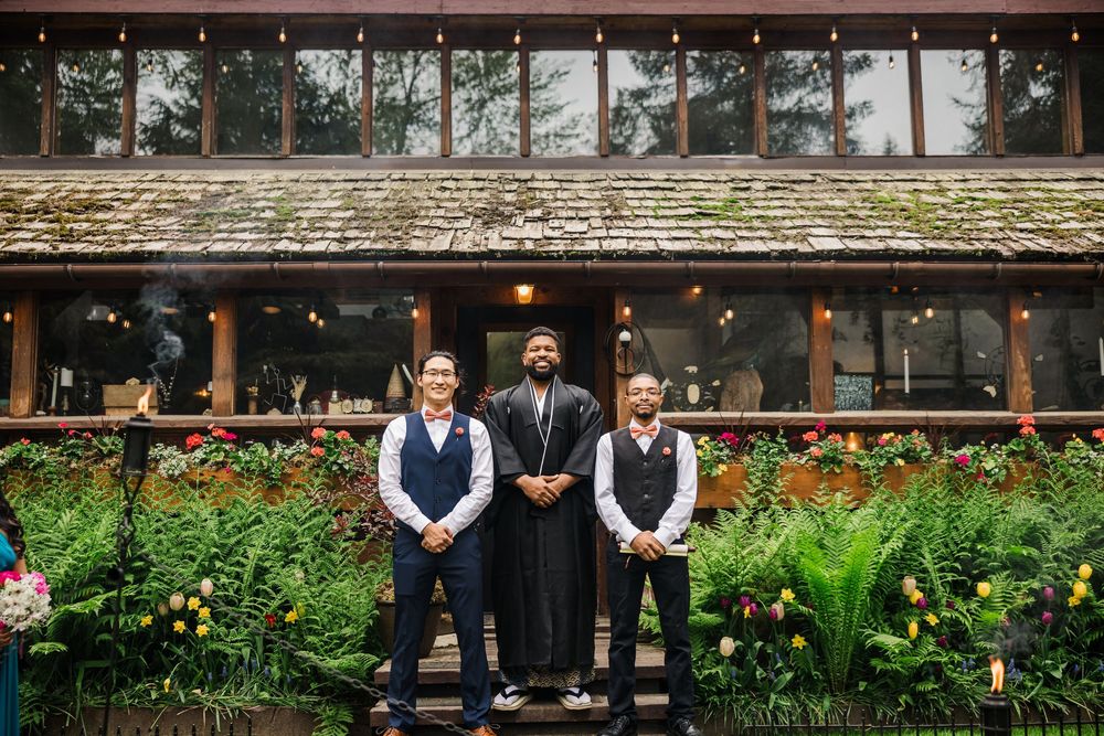 Wedding party poses in front of rustic lodge with natural garden landscaping.