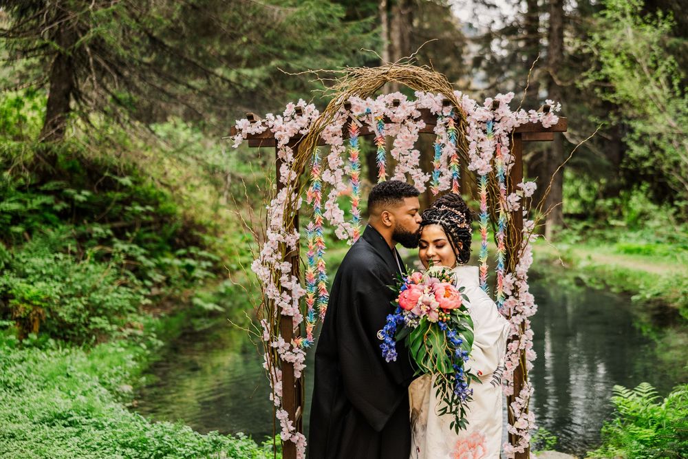 Couple sharing an intimate moment under a cherry blossom arch beside a forest stream.