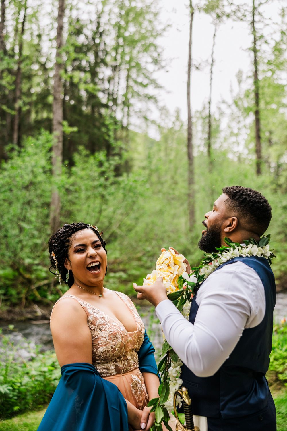 A joyful couple laughing together during their outdoor wedding photoshoot by a stream.