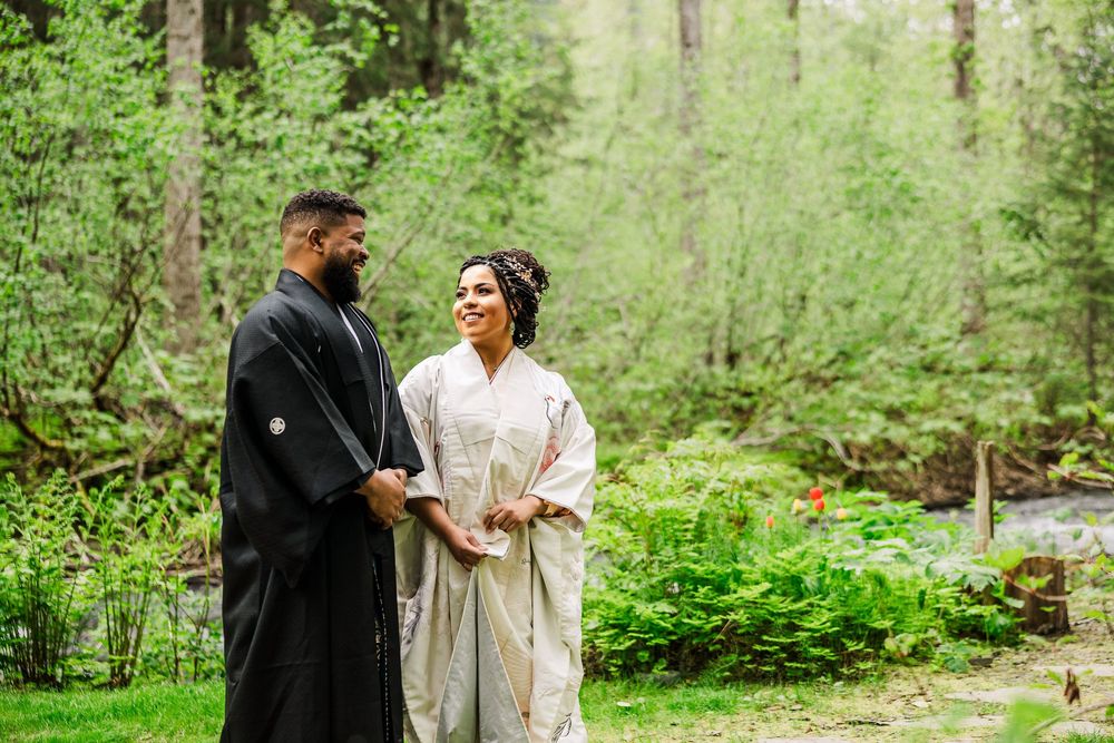 Happy couple shares joyful moment during outdoor forest wedding in traditional Japanese dress.