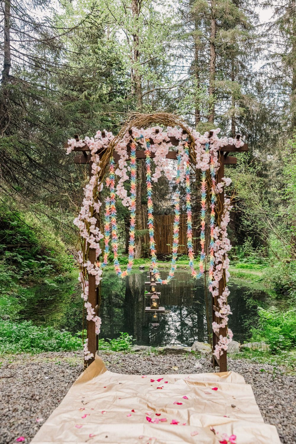 Romantic floral wedding arch decorated with pink blossoms and greenery in a forest setting.