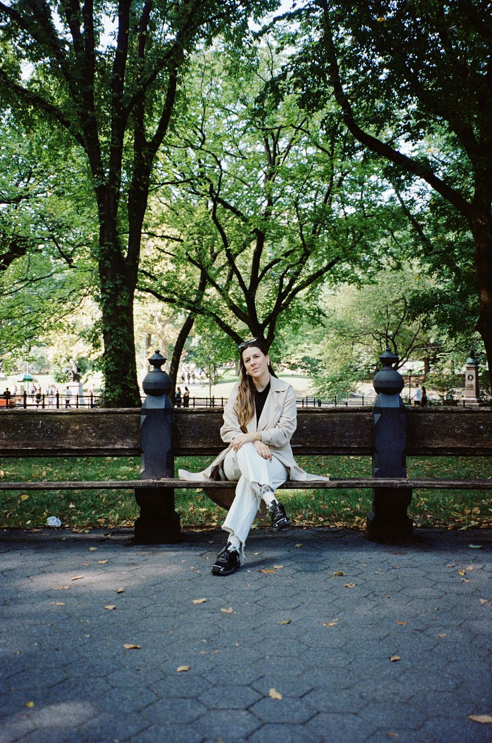 Casual outdoor portrait on a park bench surrounded by lush green trees.