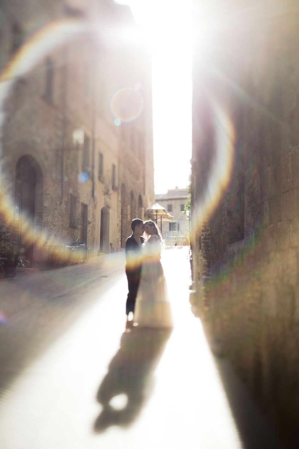 Sunlit alley in an Italian town with lens flare creating rainbow effects.
