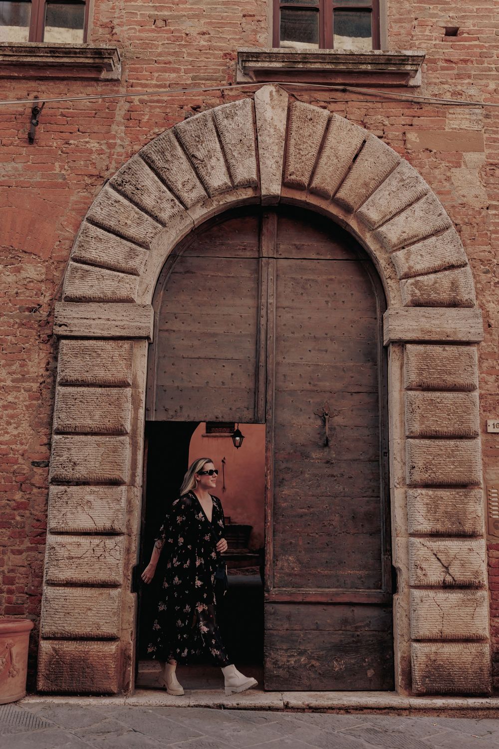 Person standing in a floral dress beneath an ornate stone archway of a historic building.