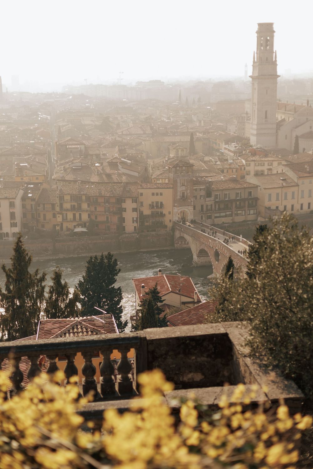 Misty cityscape view of Verona, Italy with historic buildings and tower rising above terracotta rooftops.