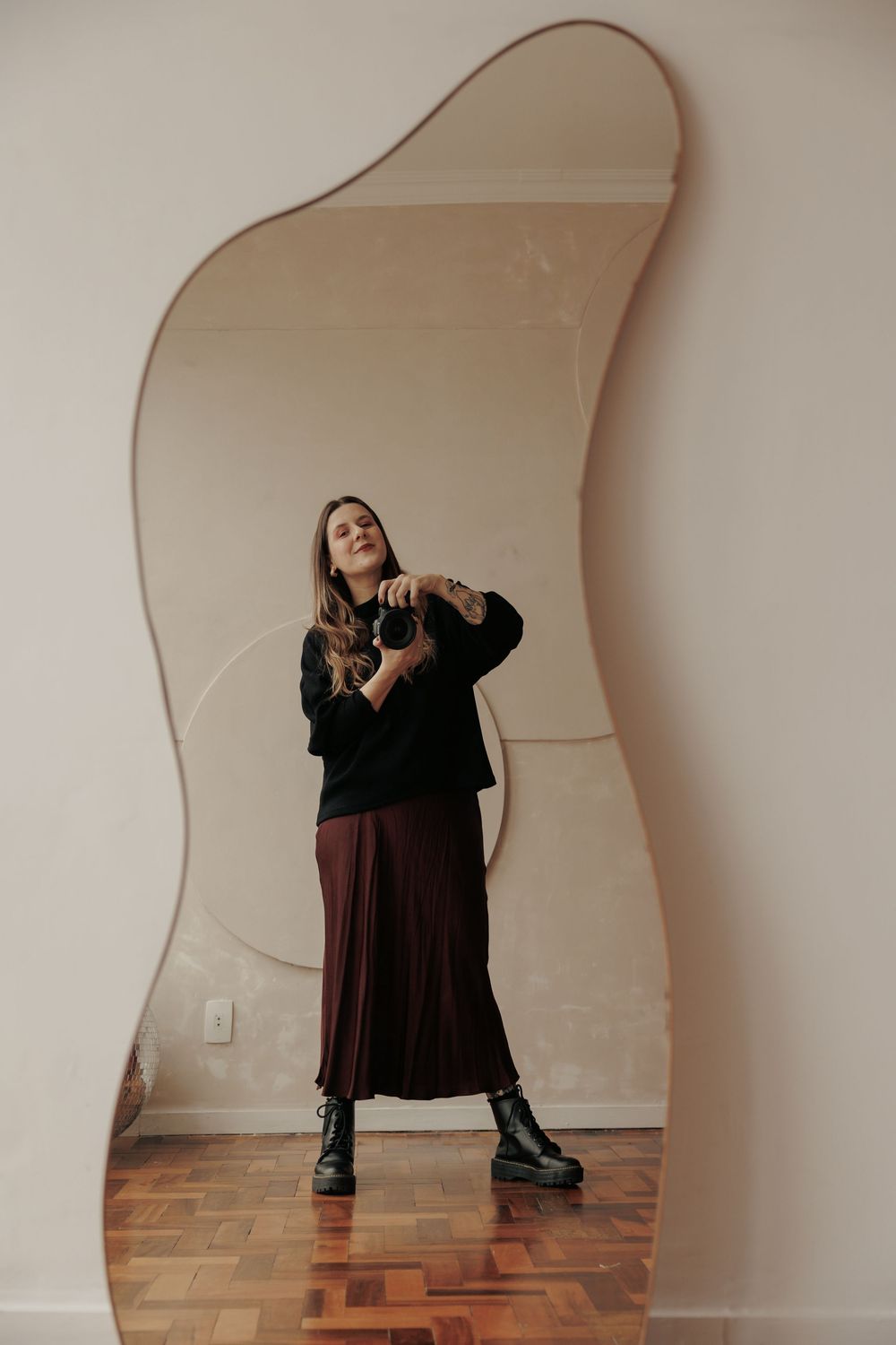 Artistic mirror reflection of a photographer in a black sweater and burgundy skirt.