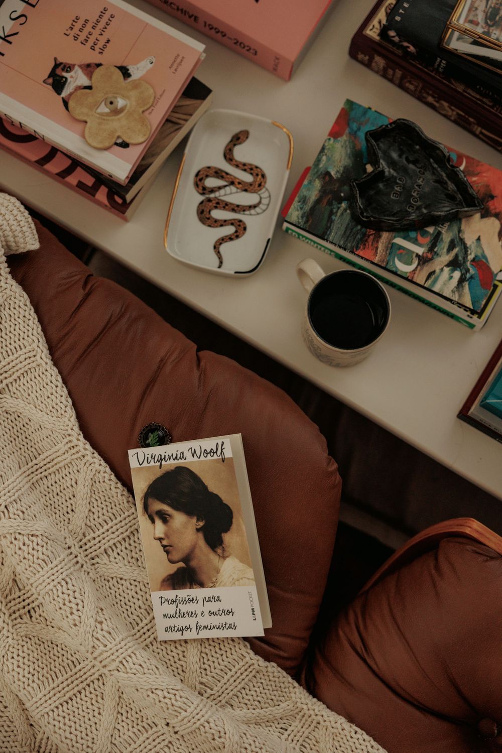 Cozy reading nook with books, snake illustration, and vintage Virginia Woolf cover.