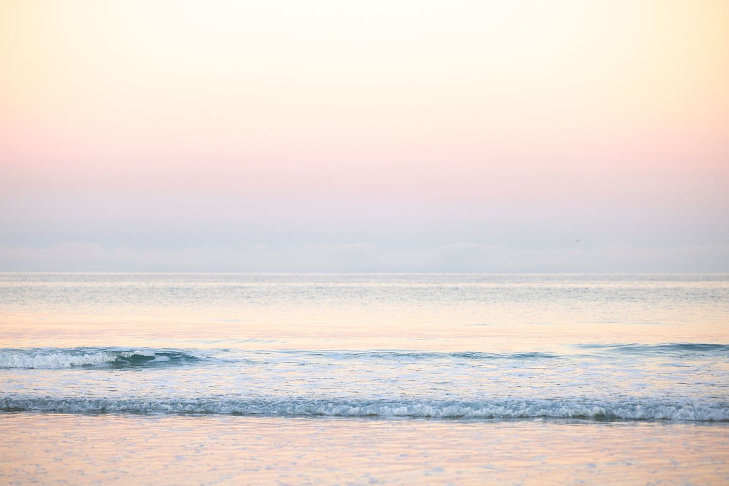 Gentle ocean waves roll onto the beach during a peaceful pastel pink and purple sunset.