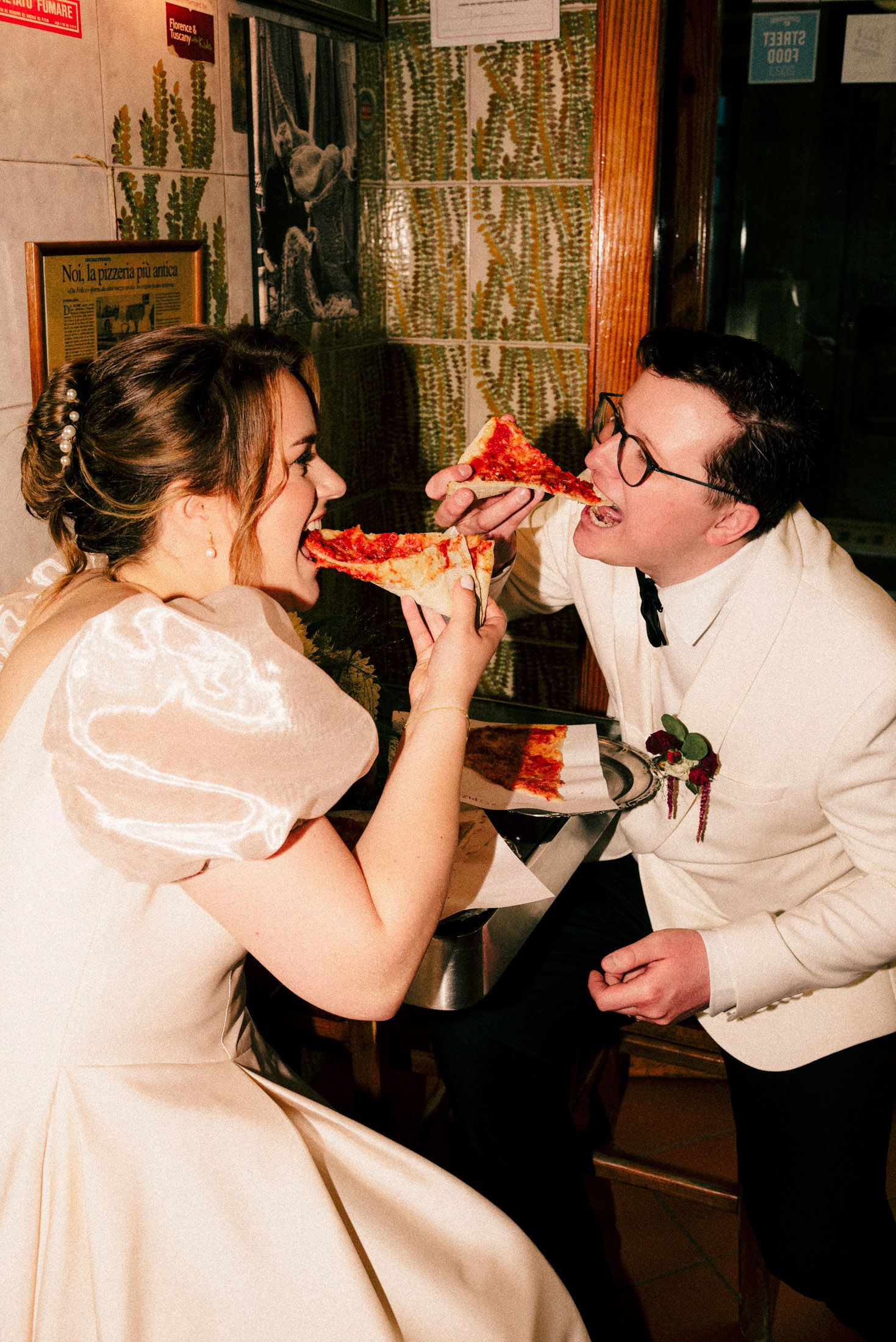 Newlyweds sharing pizza together in playful moment at reception.