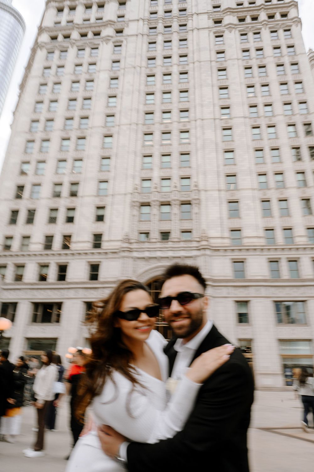 A happy couple embraces in front of a grand historic building with ornate architecture in an urban setting.