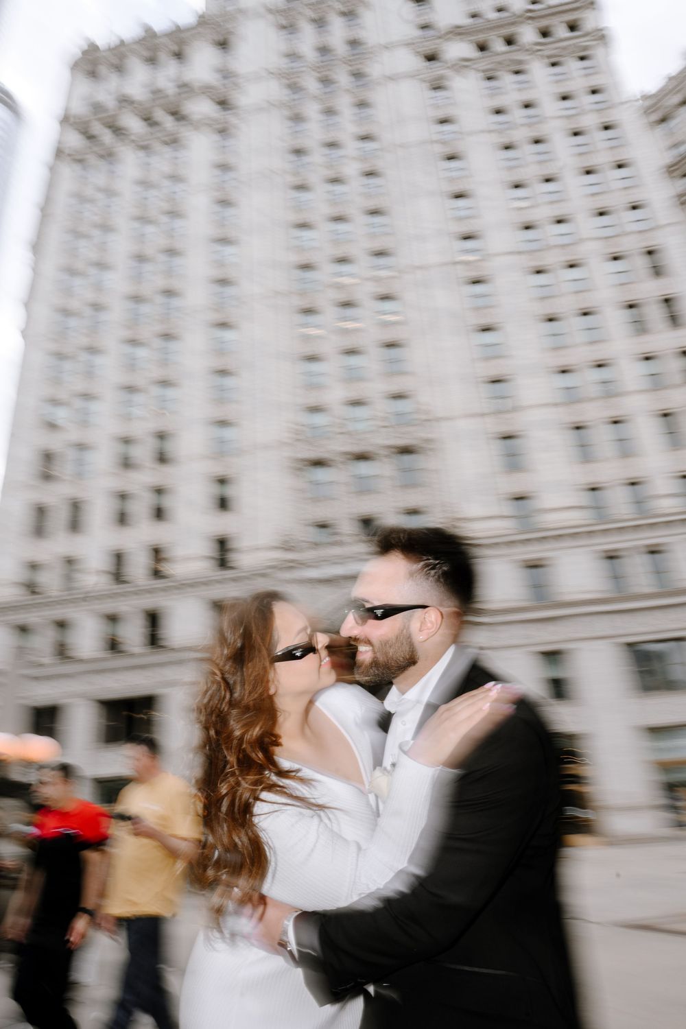 A romantic couple embraces in a motion-blurred moment outside a tall historic building in an urban setting.