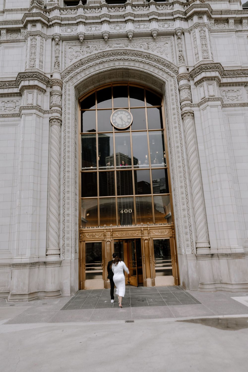 A person in white walks through the grand entrance of a historic stone building with ornate architectural details.