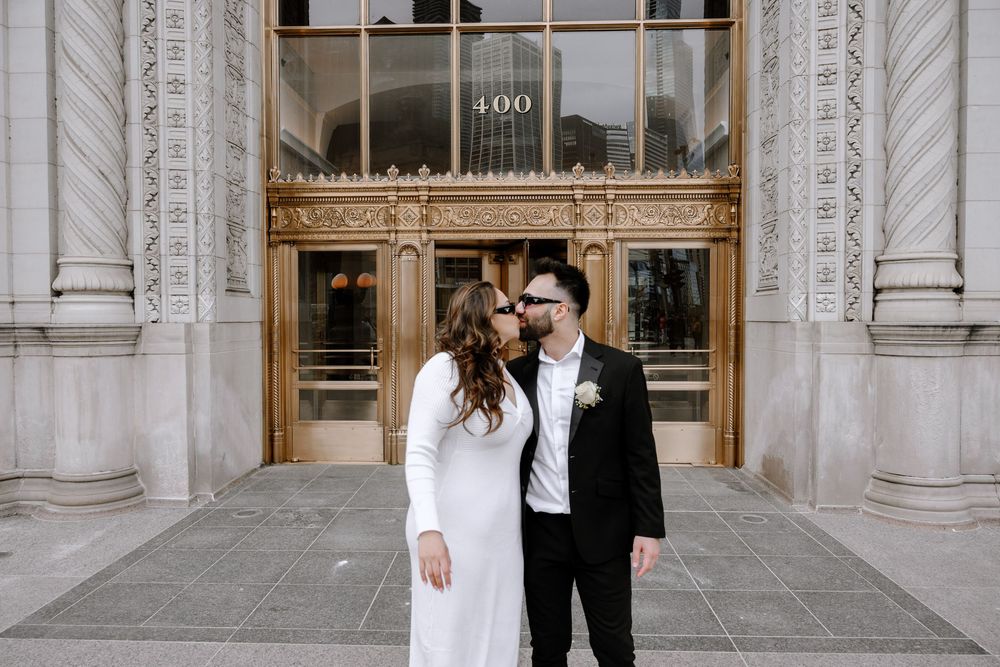 Newlywed couple stands in front of ornate courthouse entrance with classic stone columns and decorative doors.