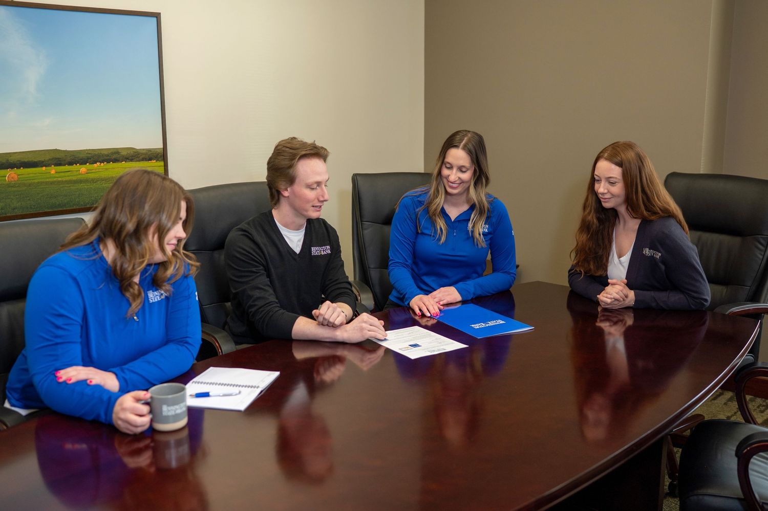 Four professionals in business attire having a discussion at a wooden conference table in an office meeting room.