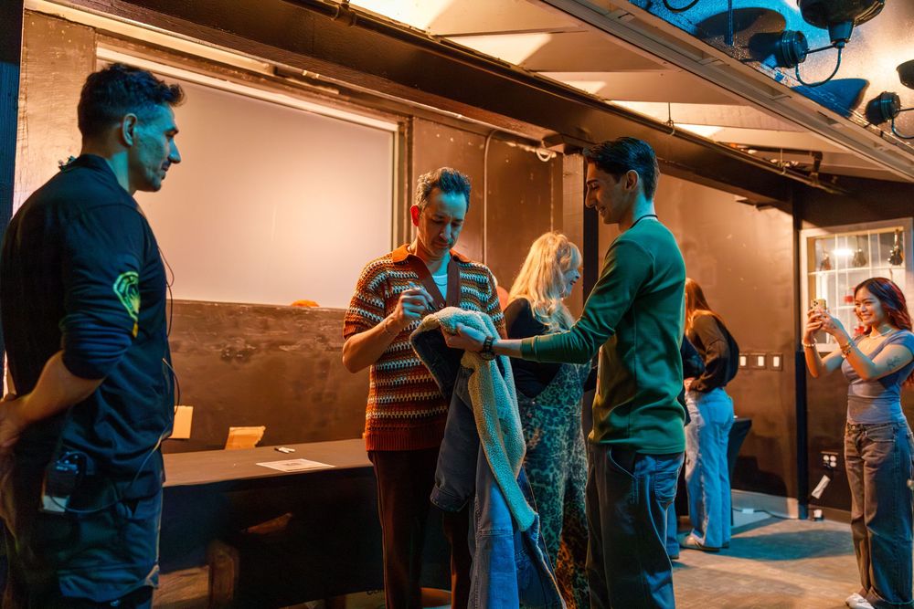 A group of people having a conversation backstage in a dimly lit area with blue lighting.