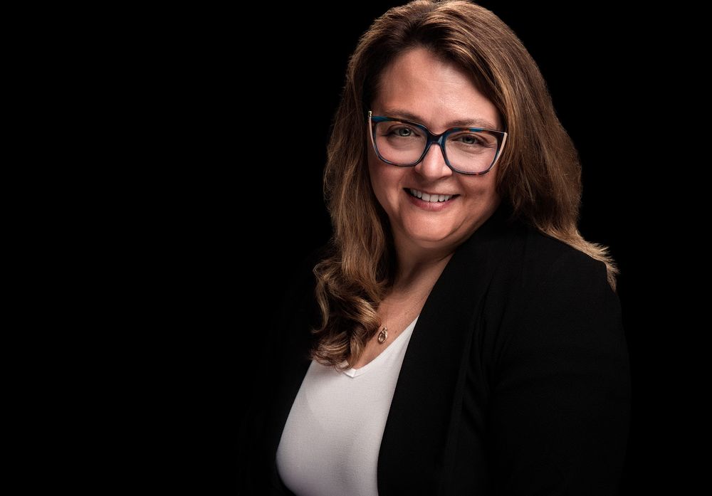 Professional business portrait with black blazer and white top against dark background.