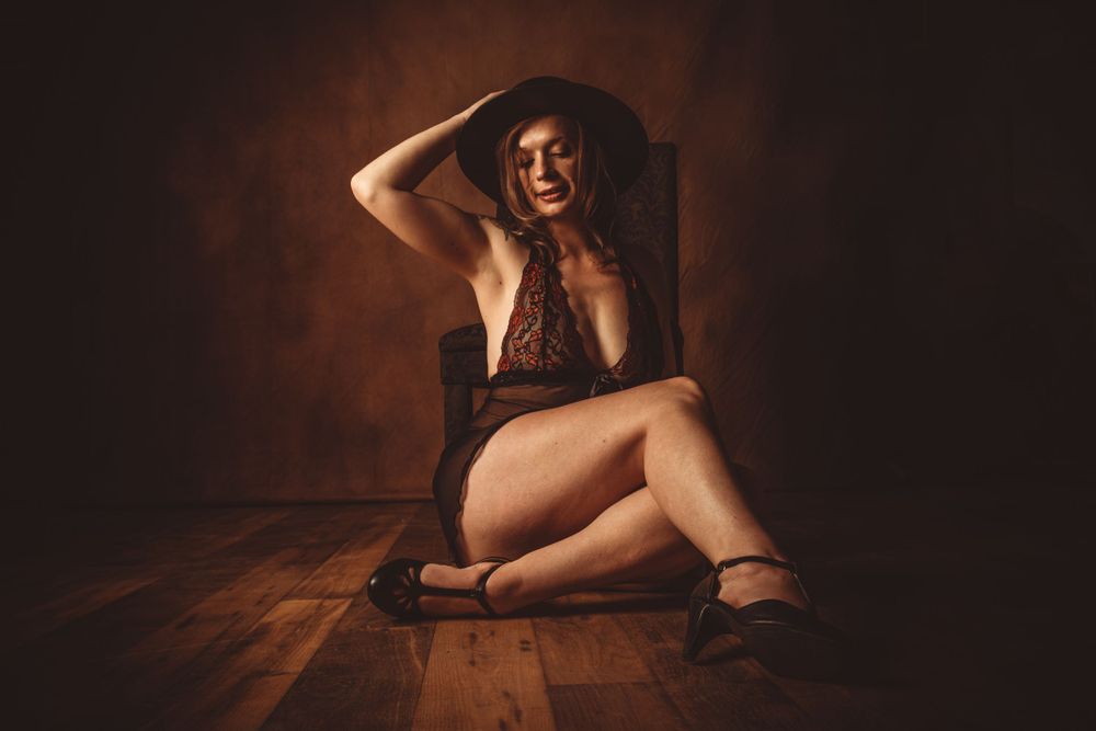Dramatic boudoir portrait in warm tones with moody lighting on wooden floor.