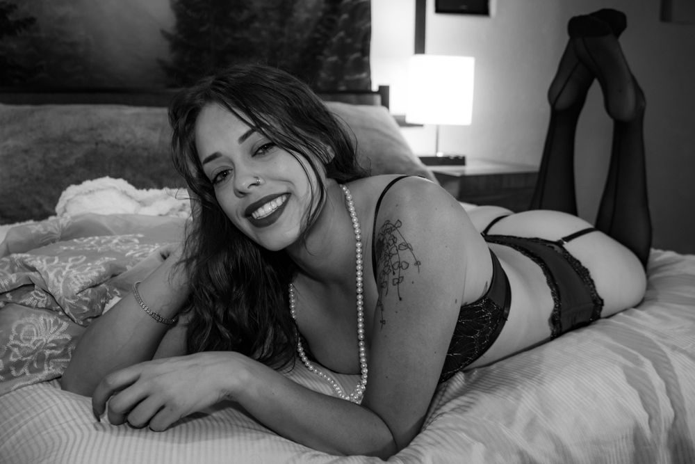 Black and white boudoir photography on bed with natural window lighting.