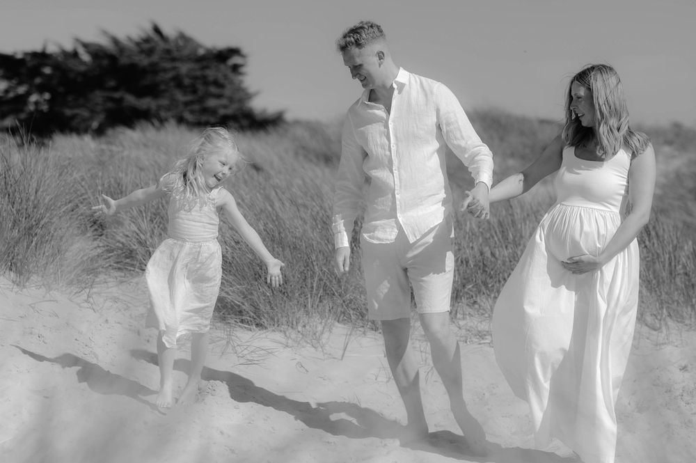 A series of black and white photographs show a couple walking together through sand dunes wearing light summer clothing.