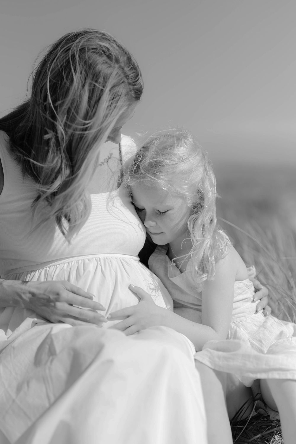 A touching black and white photograph shows a mother and young child in white dresses sharing a tender moment together.