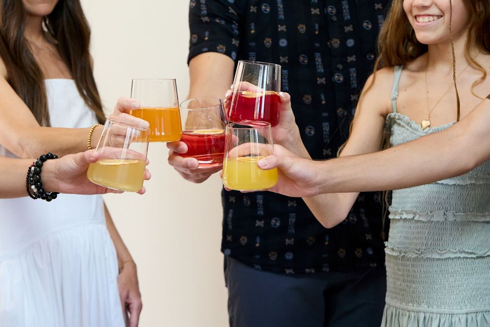 People toasting with colorful cocktails and fruit juices at a social gathering.