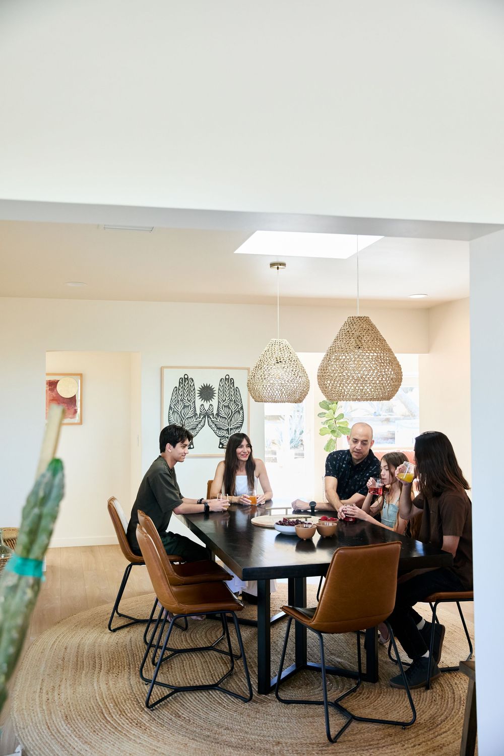 Colleagues gather around a modern dining table beneath woven pendant lights for a casual meeting in a bright office space.