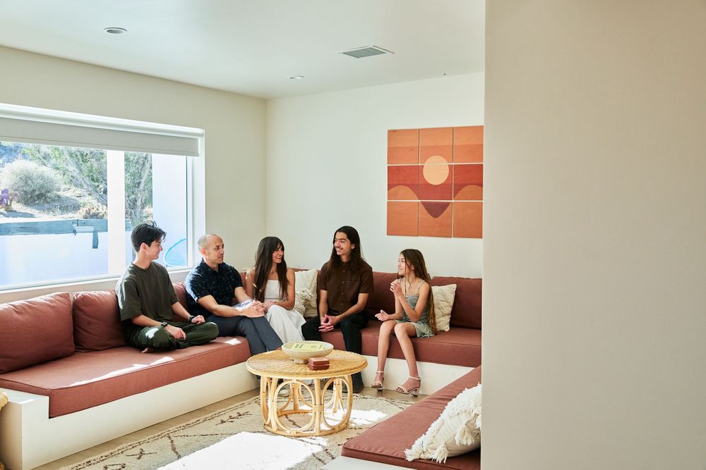 A group gathered in conversation on built-in seating around a gold coffee table beneath a retro wall art piece.