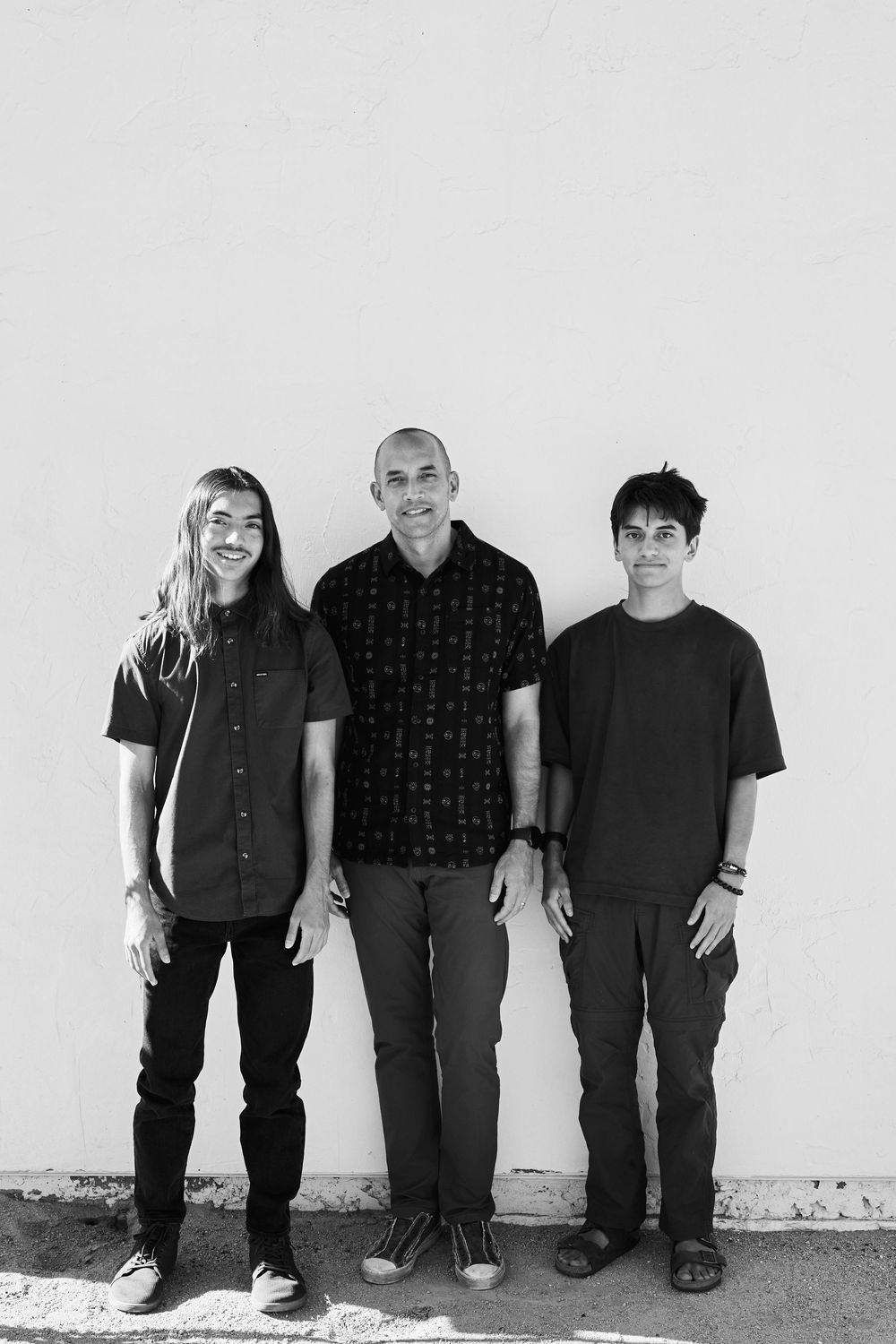 Group of people wearing dark casual clothing sitting together against a white wall in a casual portrait series.