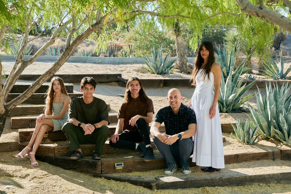 People relaxing outdoors on wooden benches surrounded by agave plants and desert landscaping on a sunny day.