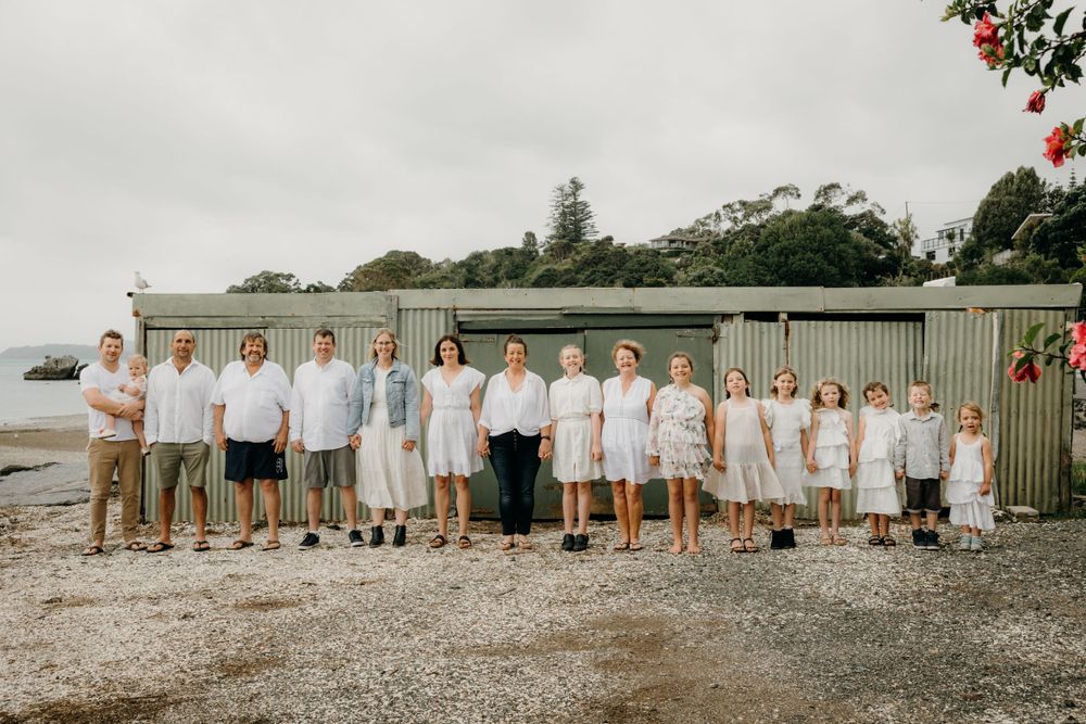 Group portrait of people dressed in white and beige standing in line against rustic building.