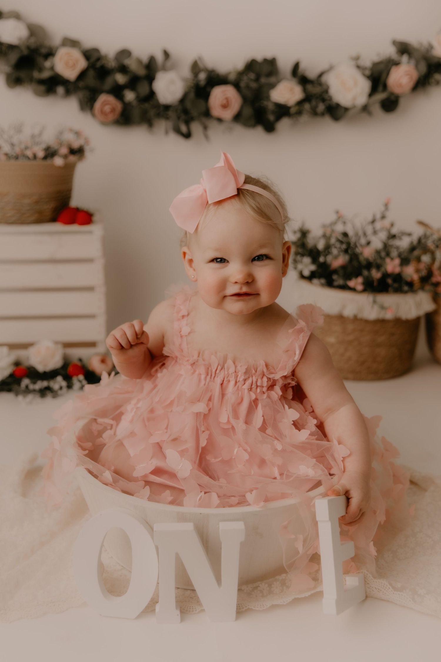 A small child in striped outfit sits on floor with white buttercream cake surrounded by floral decorations and holiday details.