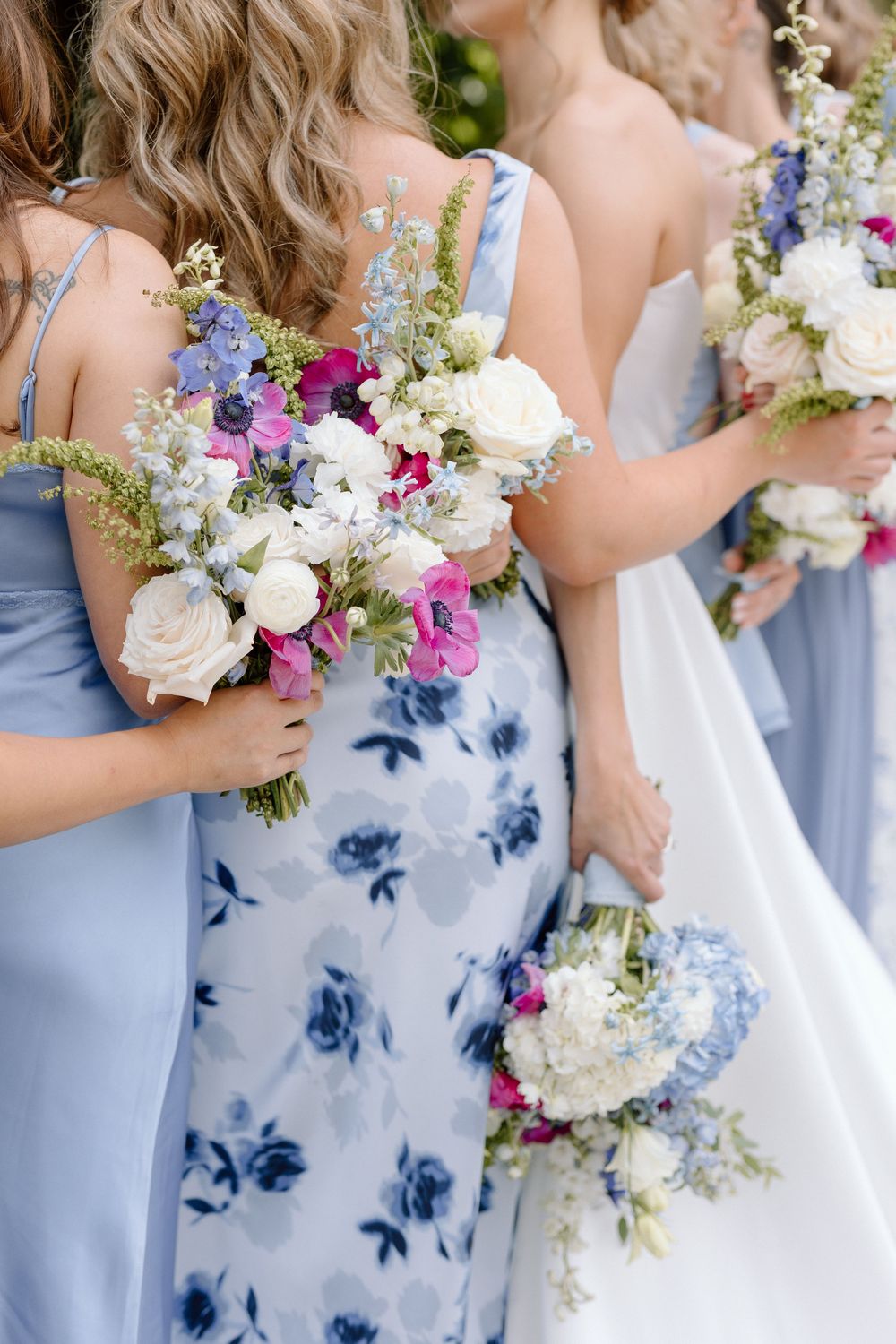 Bridesmaids carry elegant bouquets featuring white roses and pink flowers against light blue floral print dresses.