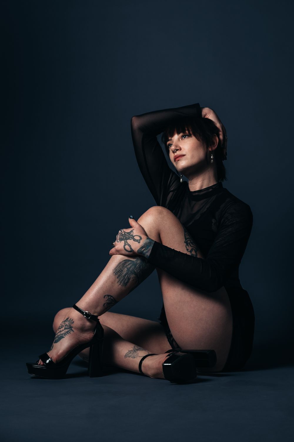 Dark artistic portrait featuring a model in black with visible tattoos.