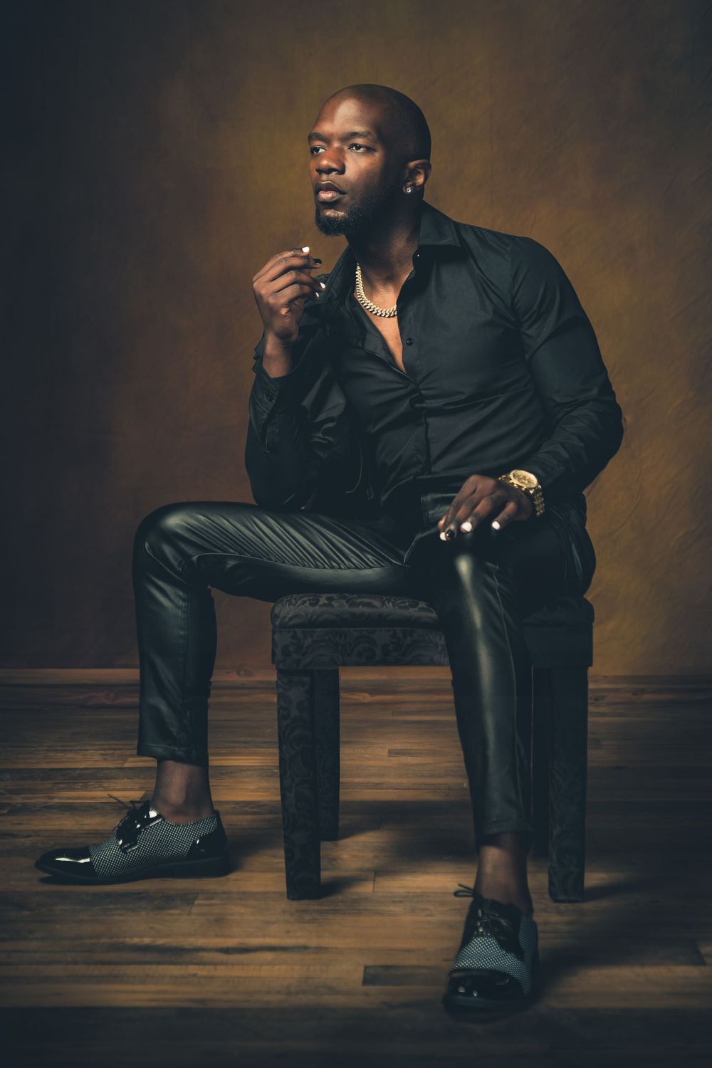 Dramatic studio portrait of a model in black shirt seated on wooden stool.