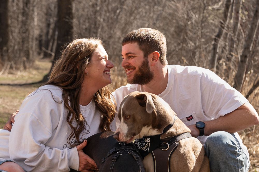 Couple shares laughter with their dog during outdoor engagement photo session.