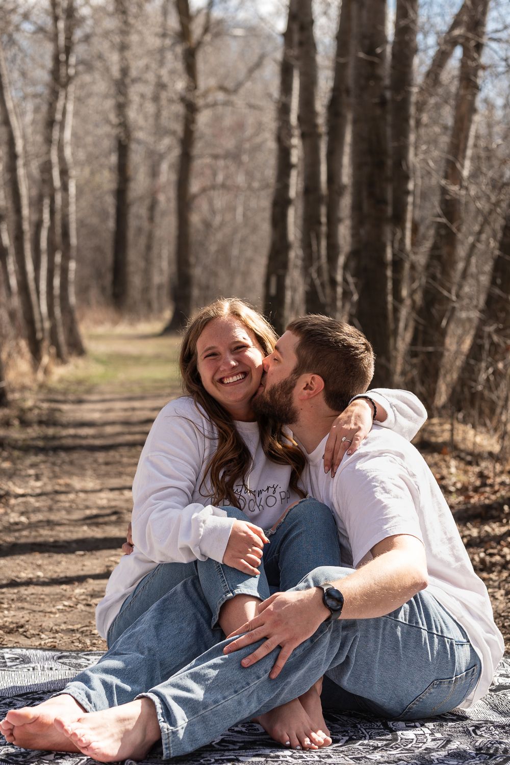 Couple laughing together while sitting on blanket in autumn forest.