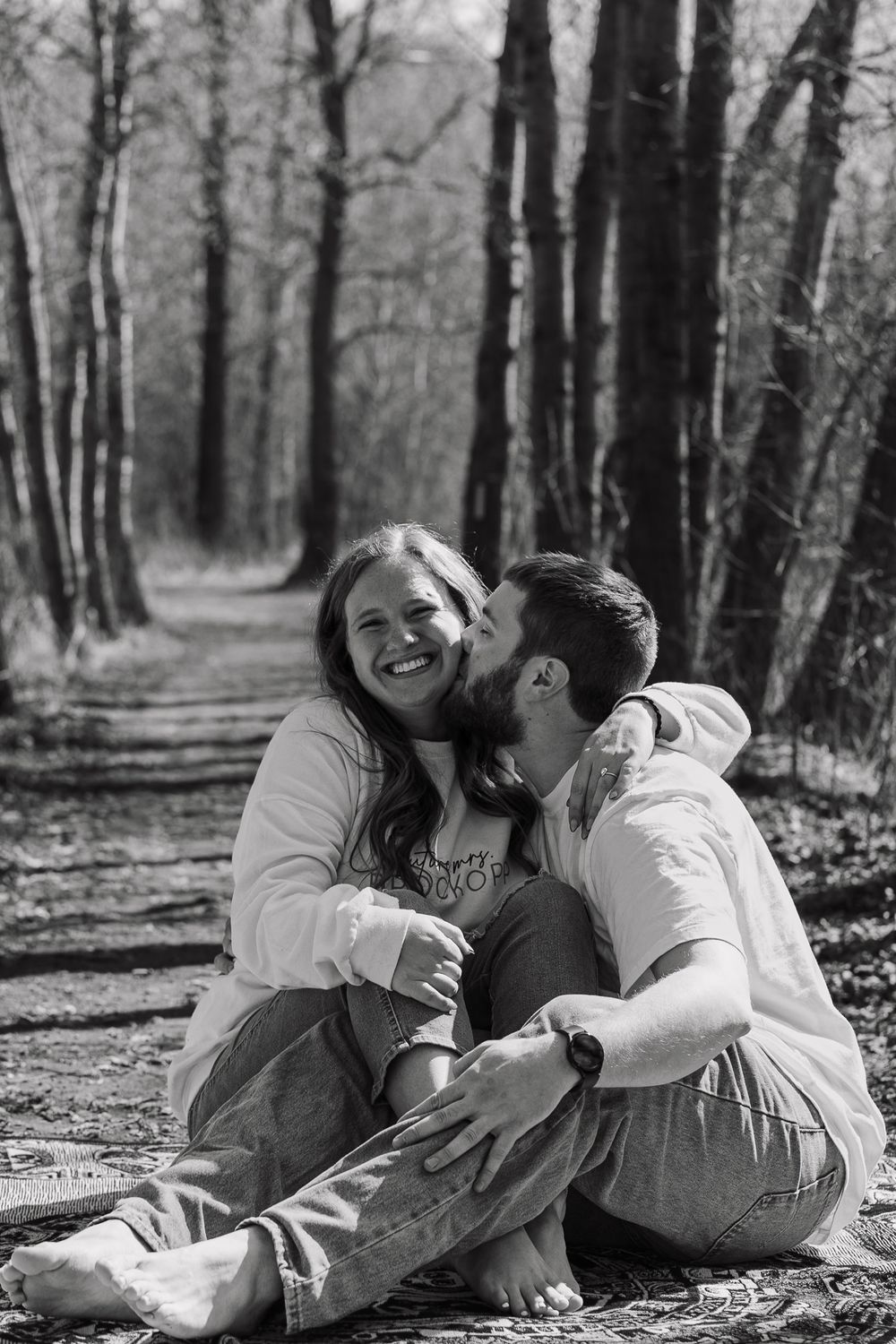 Black and white photo of couple sharing joyful moment on blanket in woods.