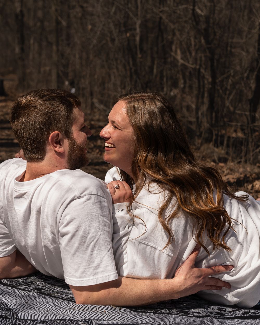 Couple in white shirts lying on blanket sharing tender moment in forest.