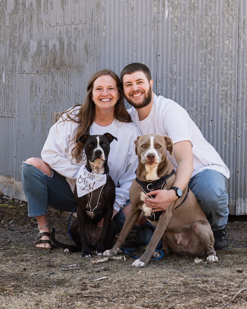 Couple with their two rescue dogs posing in front of corrugated metal wall.